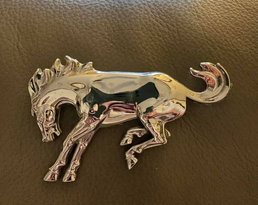 Chrome Ford Bronco bucking-horse emblem resting on brown leather, a mark of the Buck Buck Bronco tradition